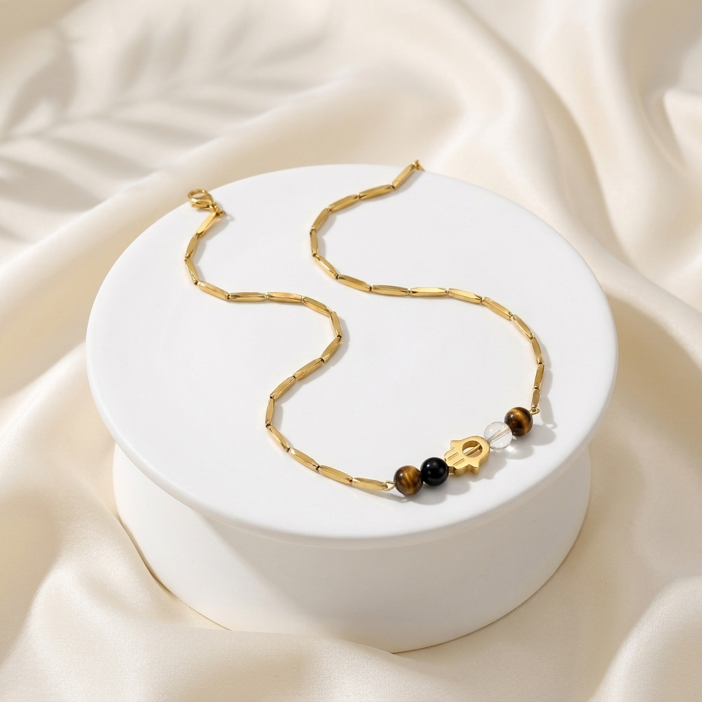 Golden Hamsa crystal rice chain necklace with Tiger Eye, Black Obsidian and Clear Quartz beads on a cream pedestal